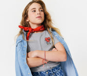 Young girl wearing a red bandana, denim jacket, and gray shirt with a heart on a skateboard  graphic on a white background